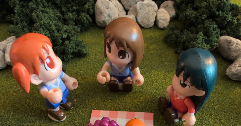 A picnic scene featuring Osaka, Sakaki, and Chiyo toys, sitting out in a grassy area someplace, with various fruits.